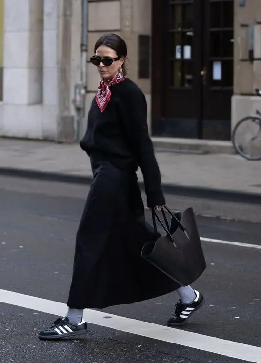 woman in black knit sweater black midi skirt red bandana tied at neck grey crew socks adidas samba black sneakers large black leather tote small black sunglasses walking street outfit 10