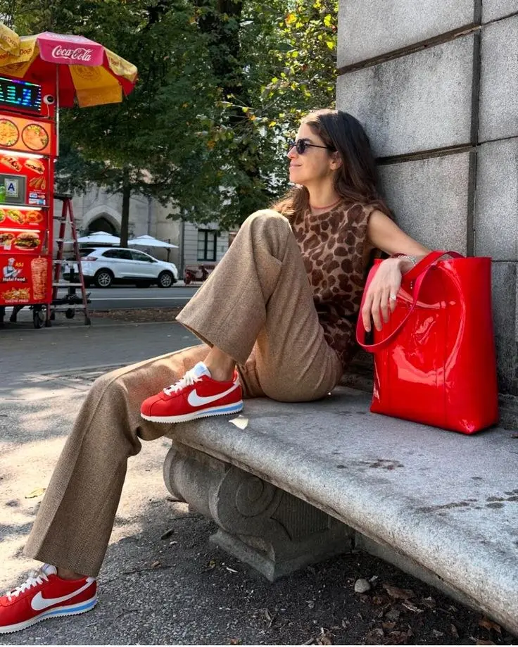 woman in leopard print sleeveless top camel wide leg trousers red Nike Cortez sneakers red patent leather tote bag sunglasses sitting outdoors outfit 5