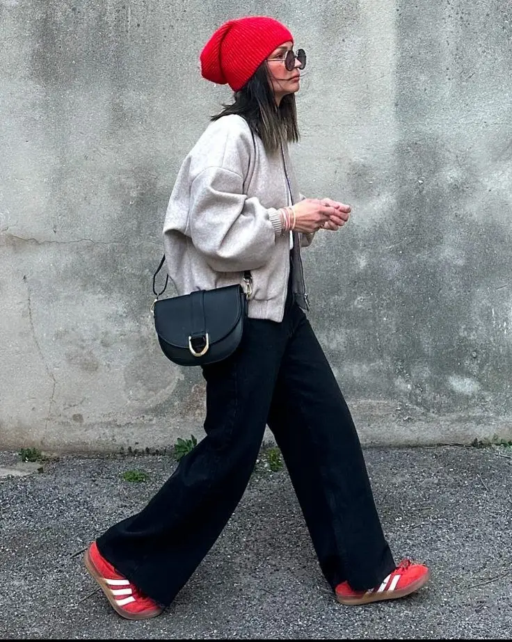 woman walking in oatmeal bomber jacket black wide leg jeans red Adidas Samba sneakers red beanie hat black crossbody saddle bag oversized sunglasses street style outfit 10