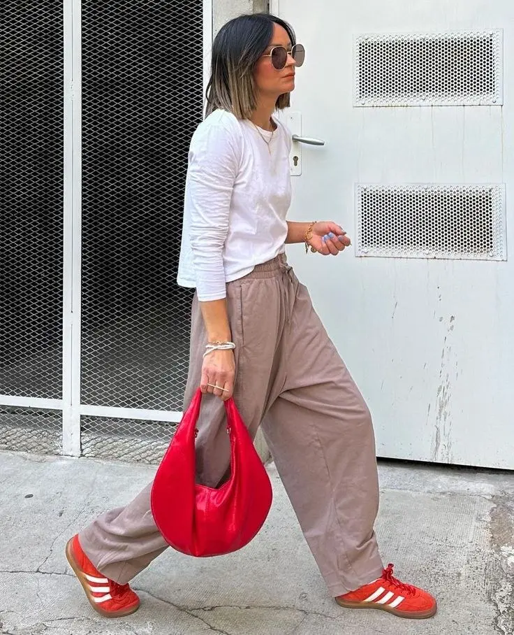 woman walking in white long sleeve tee taupe wide leg drawstring trousers red Adidas Samba sneakers red crescent bag gold sunglasses street style outfit 14