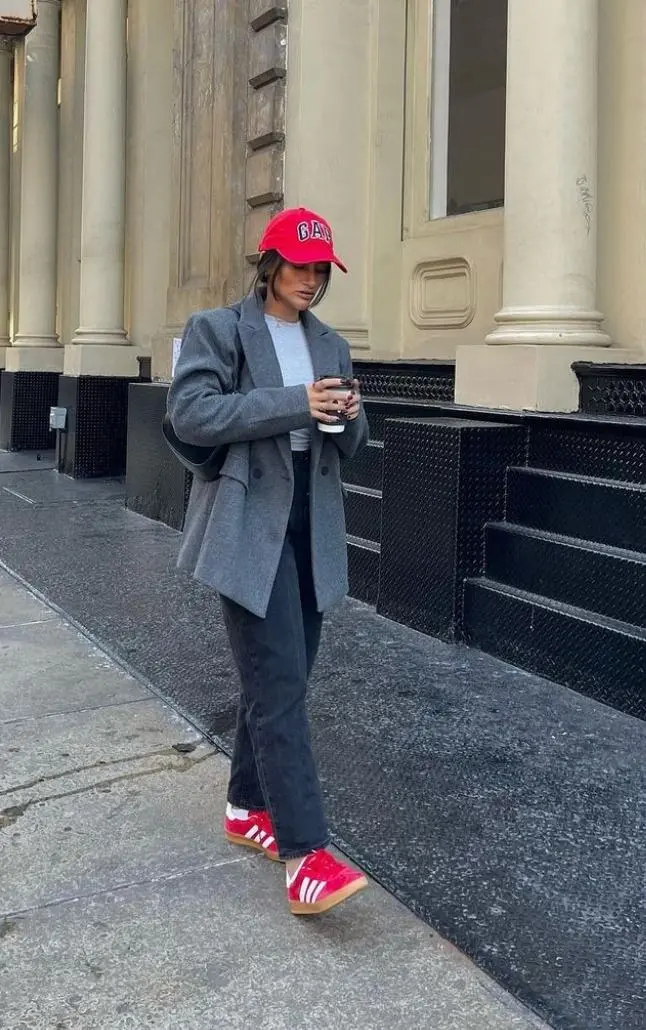 woman in red baseball cap oversized grey double breasted blazer grey tee black wide leg jeans red Adidas Samba sneakers white socks walking on wet pavement outfit 17