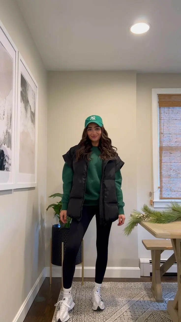 woman in green sweatshirt black puffer vest black leggings white New Balance sneakers green baseball cap outfit 1