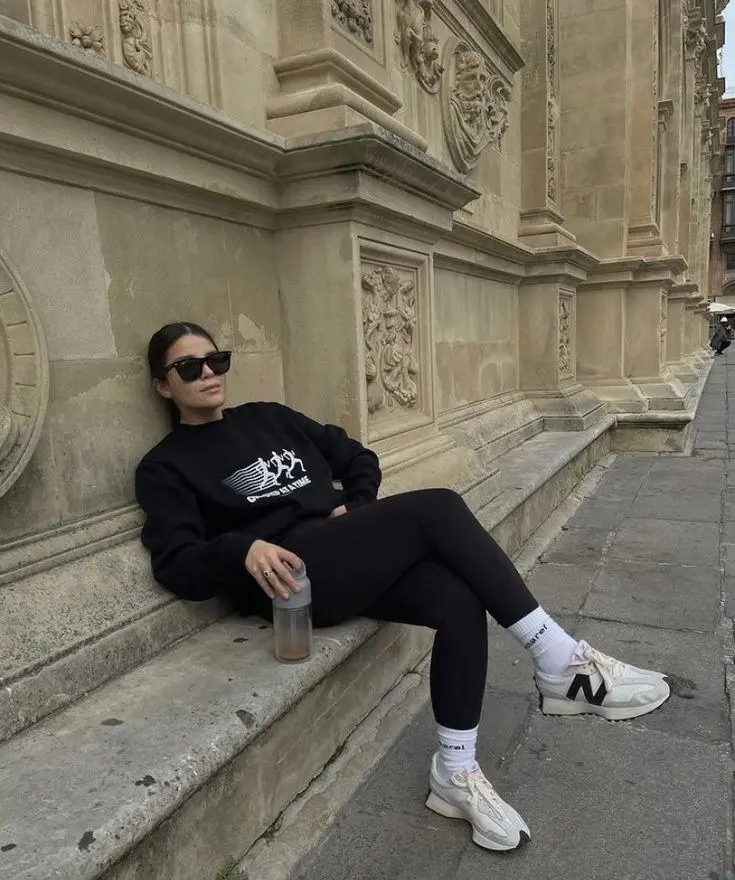 woman in black graphic sweatshirt black leggings cream New Balance sneakers sunglasses outdoor sitting outfit 2