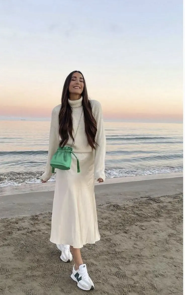 woman in cream turtleneck knit sweater ivory satin midi skirt white New Balance sneakers green bucket crossbody bag at beach sunset outfit 7