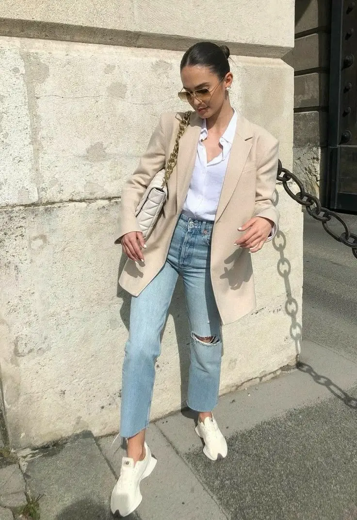 woman in beige longline blazer white shirt light wash ripped ankle jeans white New Balance sneakers quilted chain shoulder bag sunglasses outdoor outfit 9