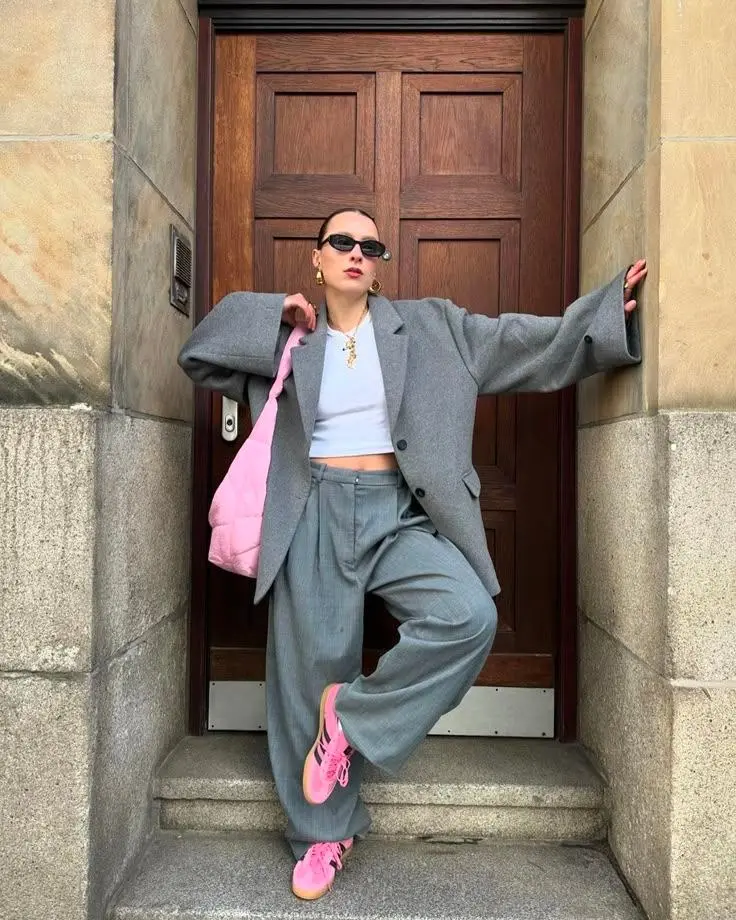 woman in large gray oversized blazer, white crop top, gray wide-leg tailored trousers, pink sneakers, pink quilted bag, gold earrings and necklace, black sunglasses, photo 3