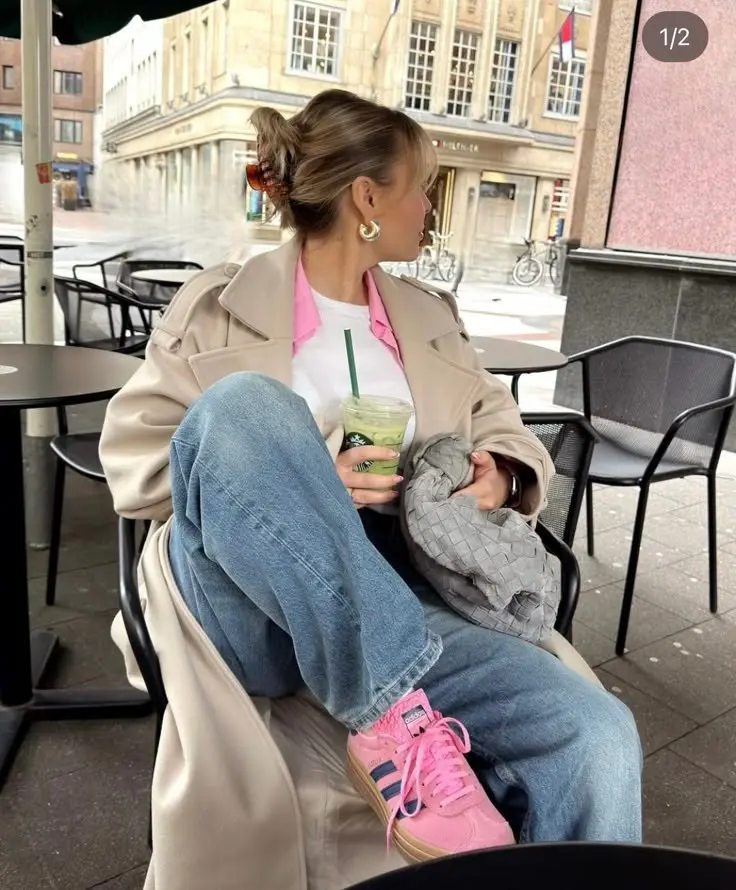 woman seated at outdoor cafe in beige trench coat, white tee, pink shirt layered underneath, baggy light wash jeans, pink sneakers, gray woven bag, hoop earrings, claw clip updo, photo 4