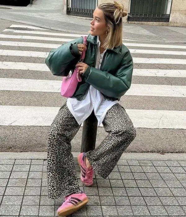 woman crouching on sidewalk in dark green leather bomber jacket, white button-down shirt, leopard wide-leg trousers, pink sneakers, small pink hobo bag, photo 12