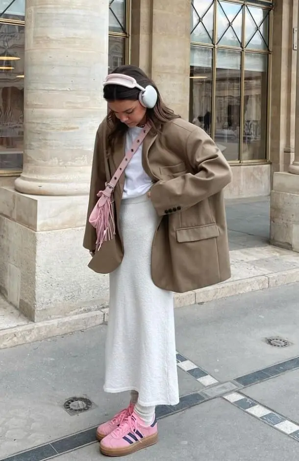 woman in oversized tan blazer, white fitted tee, white knit midi skirt, white sheer socks, pink sneakers, pink fringed crossbody bag, pink headband with headphones, photo 16