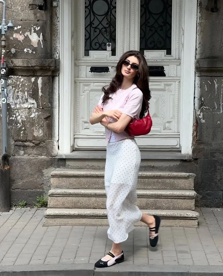 woman in pink short-sleeve cardigan white tee white polka-dot midi skirt black platform Mary Jane ballet sneakers red crescent bag cat-eye sunglasses street outfit photo 3