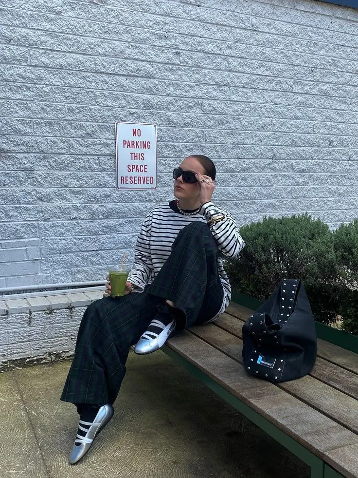 woman seated on bench in black white Breton stripe long-sleeve top dark green tartan wide-leg trousers silver metallic ballet sneakers black studded hobo bag chunky sunglasses gold jewelry photo 14