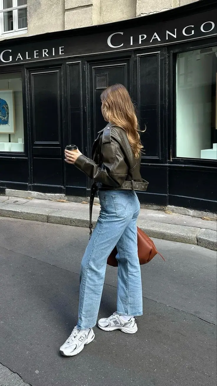 woman from behind wearing dark olive leather moto jacket light wash straight leg Levi jeans New Balance 530 white silver sneakers cognac bag outfit 4