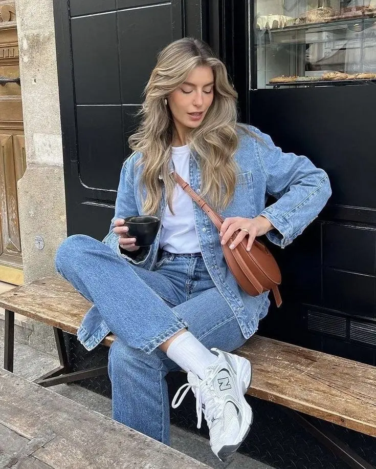 blonde woman sitting outside bakery wearing oversized medium wash denim shacket white tee straight leg blue jeans white socks New Balance 530 white silver sneakers cognac oval bag outfit 8