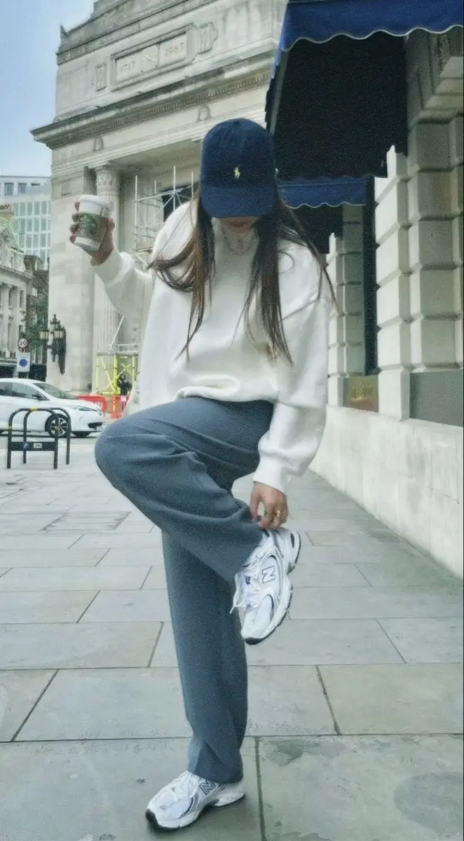brunette woman wearing navy baseball cap white pullover sweatshirt slate blue-grey wide leg trousers New Balance 530 white chunky sneakers street outfit 10