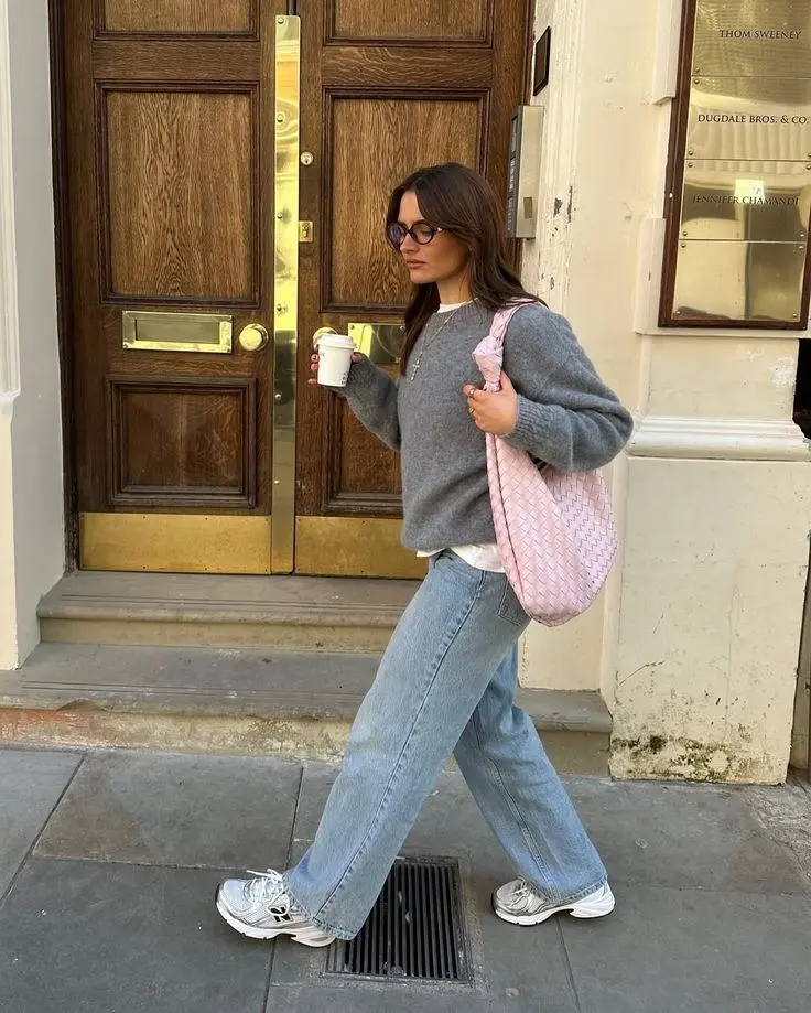 brunette woman walking wearing grey oversized knit crewneck sweater wide leg light wash jeans New Balance 530 silver sneakers large pink woven hobo bag oval glasses outfit 12