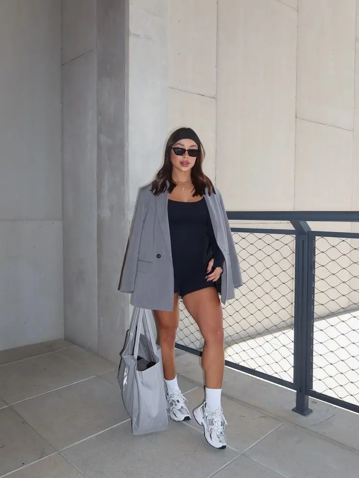 brunette woman wearing grey oversized blazer black mini bodysuit dress black headband white crew socks New Balance 530 silver chunky sneakers large grey tote bag outfit 14