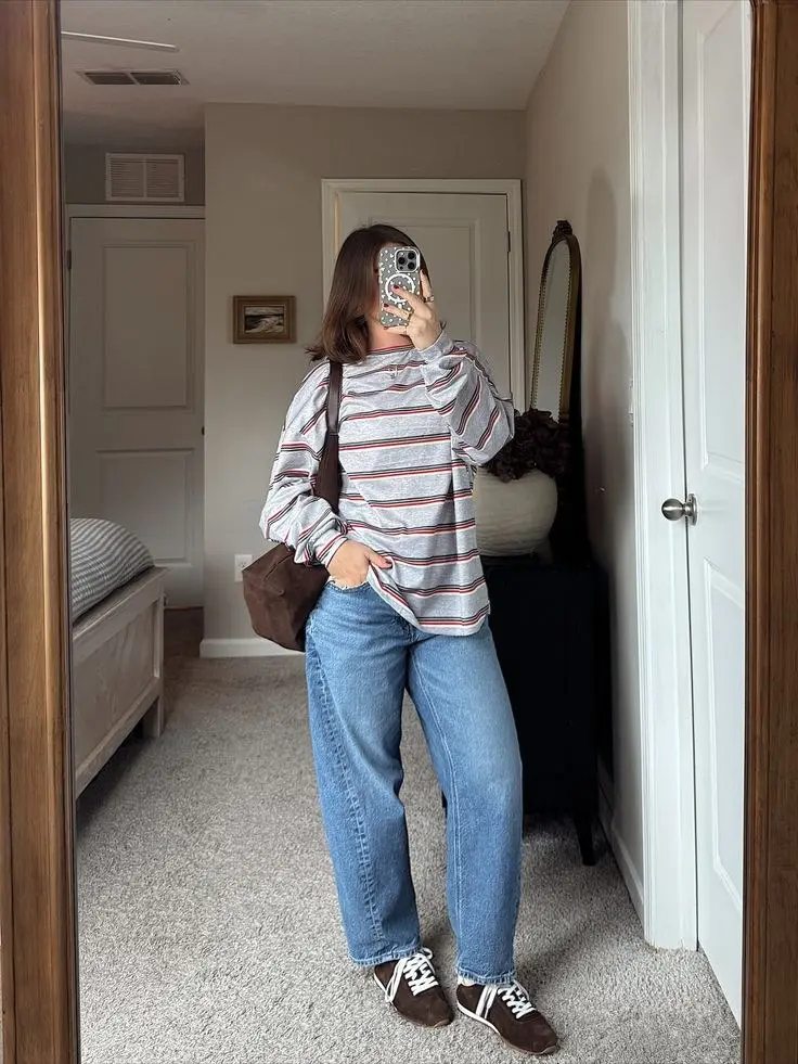 brunette woman in grey red and white striped long sleeve t-shirt light wash straight jeans dark brown athletic sneakers small brown shoulder bag mirror selfie bedroom outfit 13