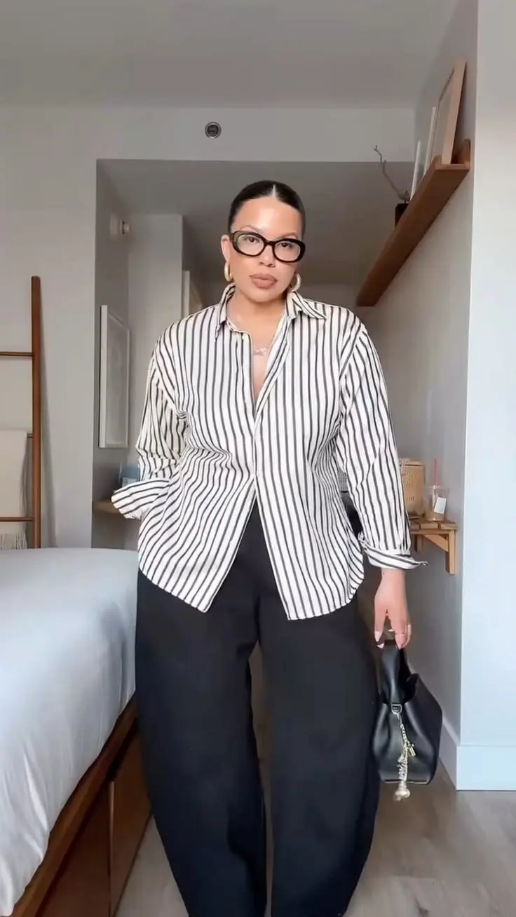 curvy woman in oversized black and white stripe shirt half tucked into wide black trousers with black bag and statement glasses outfit 2