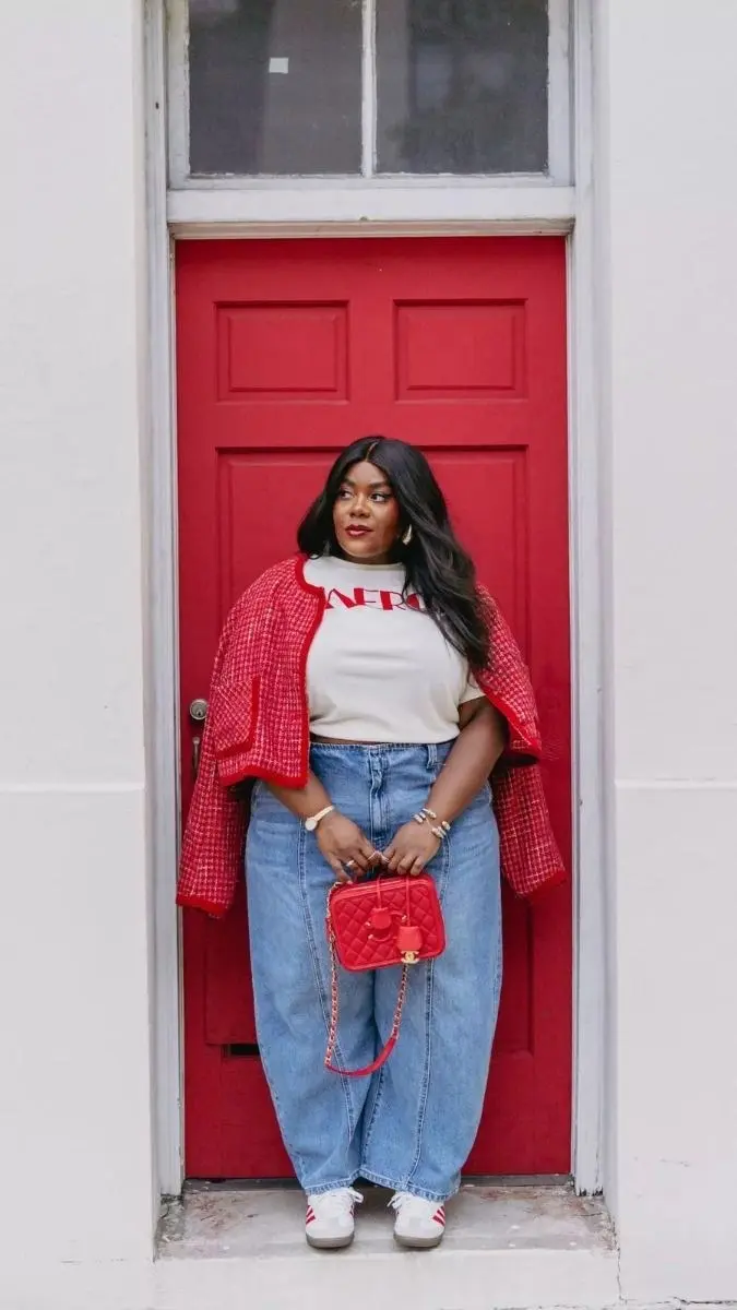 curvy woman in red boucle jacket graphic tee baggy light wash jeans white sneakers and red quilted bag standing at red door outfit 3