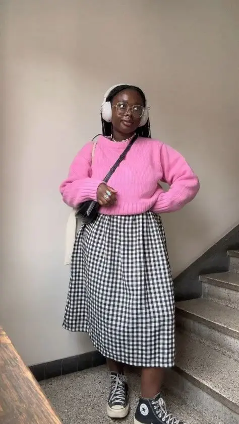 curvy woman in pink chunky knit sweater over white collared shirt black white gingham midi skirt high top Converse sneakers crossbody bag and clear frame glasses staircase outfit 13