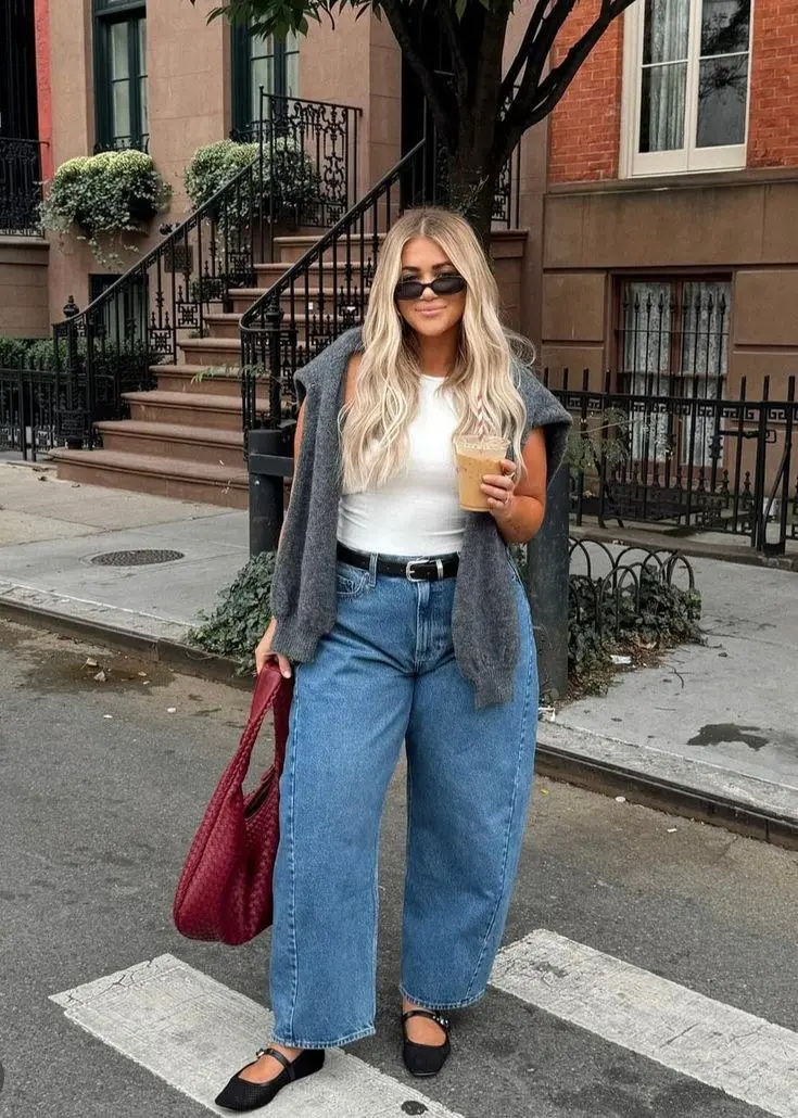 curvy blonde woman in gray knit open vest white tank wide leg mid wash jeans black belt black mary jane flats and burgundy woven bag street crossing outfit 14