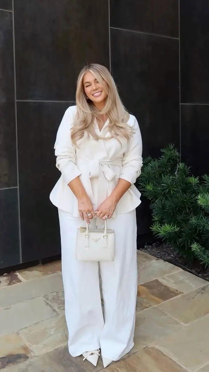 curvy blonde woman in ivory wrap blazer wide leg ivory trousers white pointed heel shoes and small cream structured bag outdoor stone terrace outfit 16