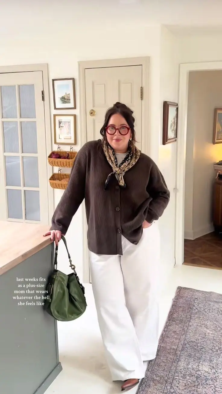 curvy brunette woman in chocolate brown ribbed cardigan printed silk neck scarf white wide leg trousers brown mules red circular glasses and olive green leather bag home kitchen outfit 18