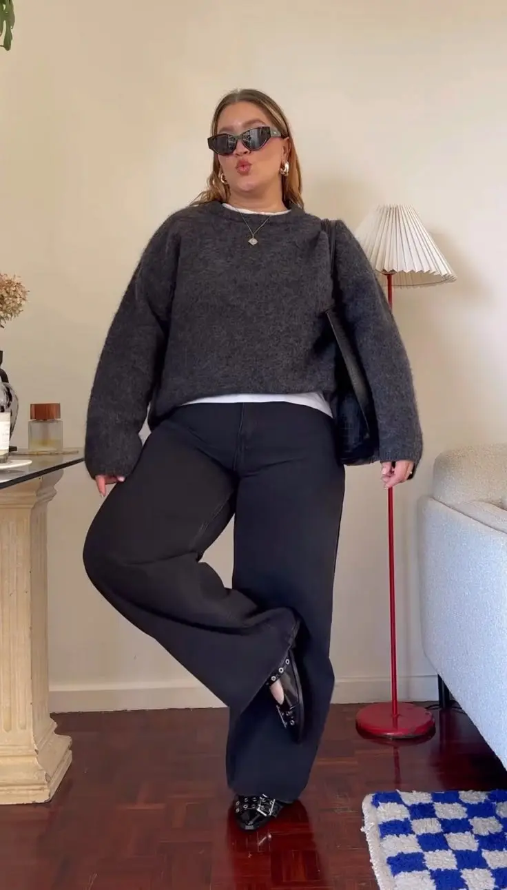 curvy blonde woman in charcoal fuzzy oversized crewneck sweater white tank layered underneath barrel wide black jeans patent black mary jane shoes small sunglasses gold earrings indoor home setting outfit 22