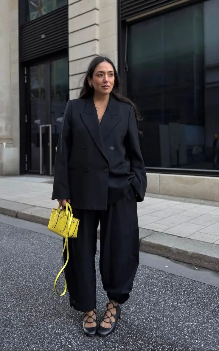 woman in oversized black double breasted blazer wide leg black trousers black lace up ballet flats neon yellow mini handbag gold hoop earrings delicate necklace outfit 3