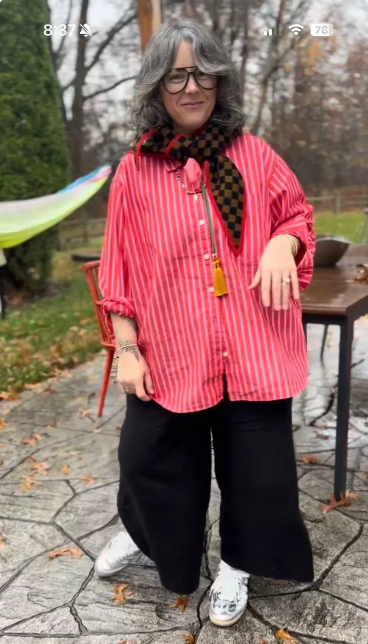woman in oversized red white pinstripe shirt black brown checker scarf tassel zip detail black wide leg jeans white vintage sneakers aviator glasses outdoor garden setting outfit 14