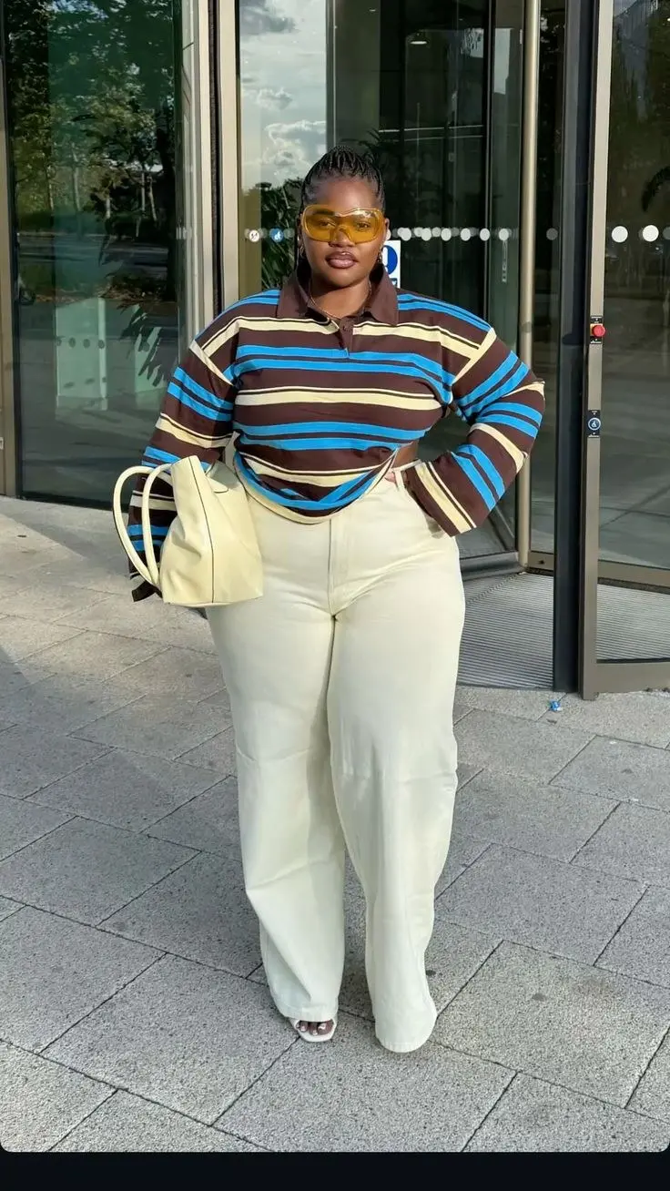 woman in brown blue cream striped rugby long sleeve polo shirt cream wide leg trousers white mule sandals cream structured tote bag yellow tinted wraparound sunglasses outdoor glass building outfit 19