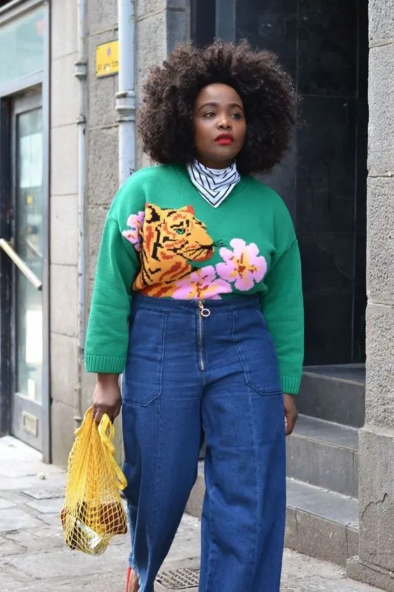 woman in kelly green tiger floral intarsia knit sweater black white stripe turtleneck high waist wide leg blue denim trousers yellow mesh net tote bag red shoe accent afro hairstyle red lip outfit 22