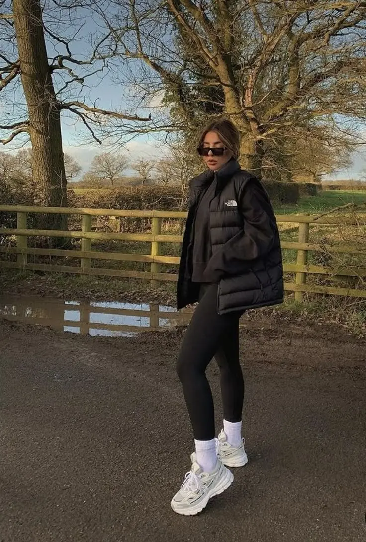 woman in black puffer jacket black leggings white socks chunky sneakers walking on country road photo 1
