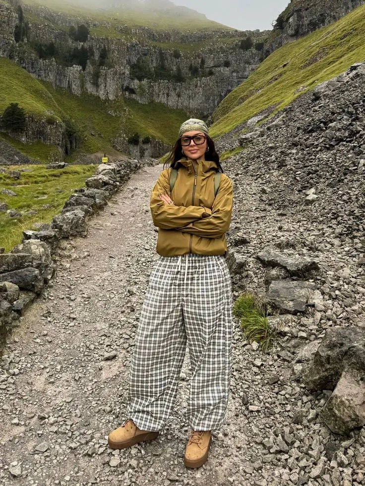 woman in olive shell jacket plaid wide leg green white trousers tan lug sole boots patterned knit beanie thick frame glasses on rocky mountain trail photo 11