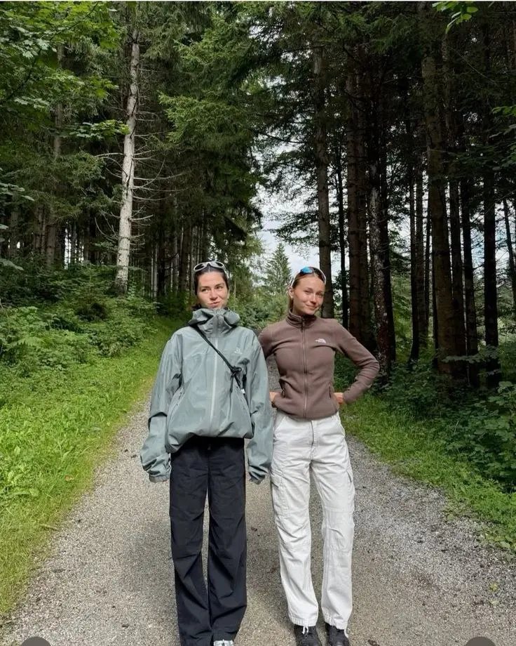 two women on forest path one in grey-blue shell jacket black wide pants one in brown North Face zip fleece white cargo pants sunglasses sport style photo 13