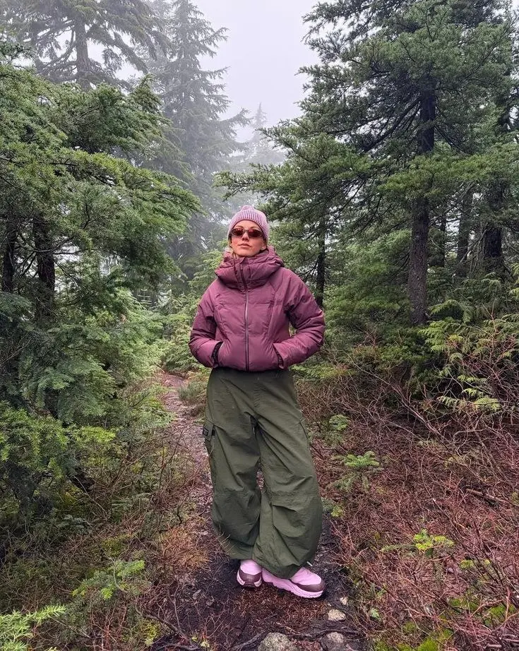 woman in mauve cropped puffer jacket wide olive cargo pants pink knit beanie pink sunglasses lavender chunky sneakers on misty mountain trail in pine forest photo 17
