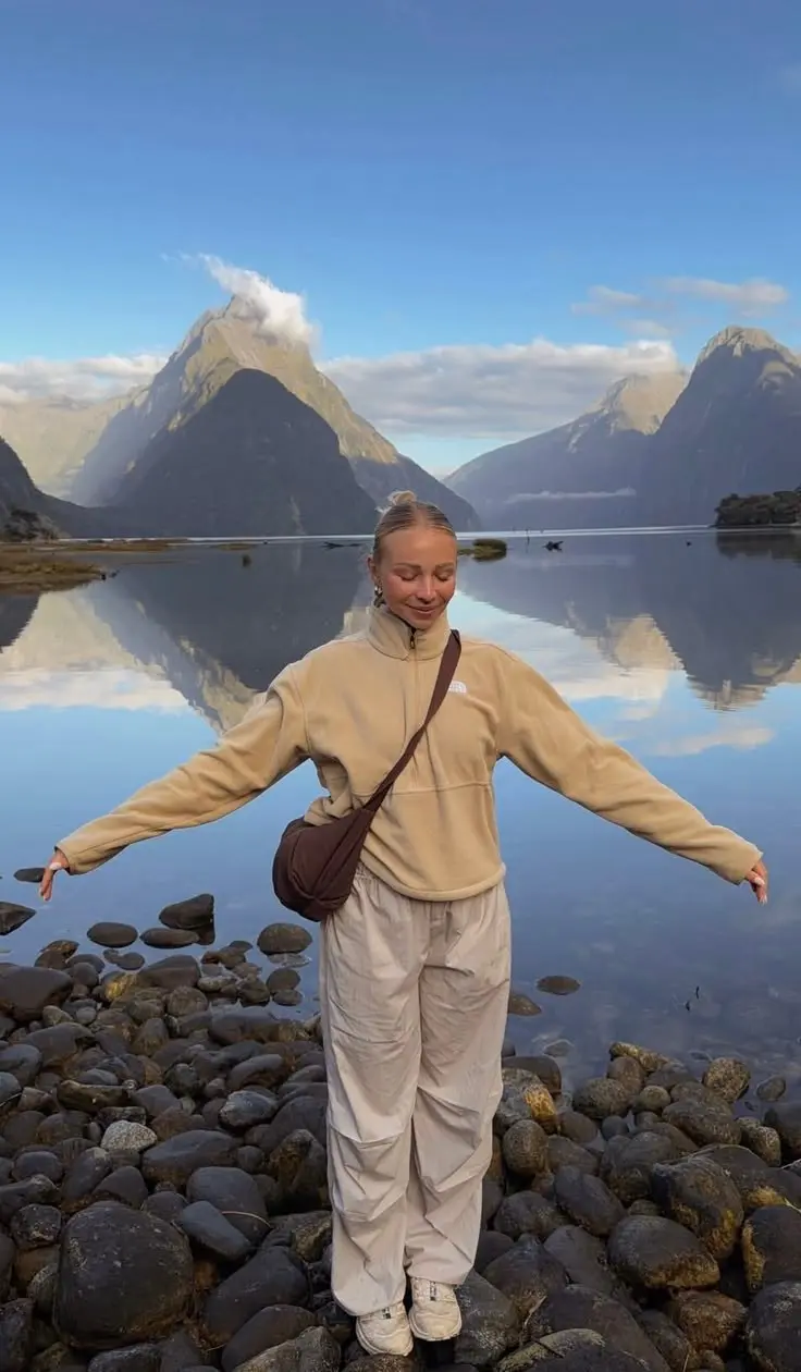 woman in camel fleece quarter zip wide cream parachute trousers brown crossbody bag white sneakers standing by reflective lake with mountains photo 18