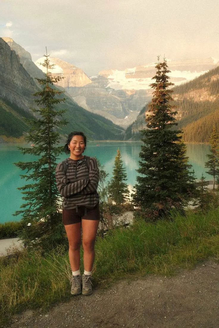woman in grey brown striped long sleeve sweatshirt dark brown biker shorts hiking shoes white crew socks smiling with backpack by turquoise lake and mountains photo 21