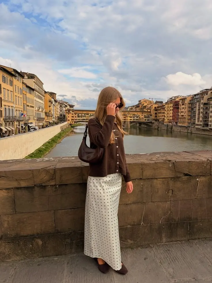 woman wearing dark brown turtleneck button front knit cardigan cream polka dot satin midi skirt dark brown suede ballet flats brown moon shoulder bag outdoor bridge setting outfit 7