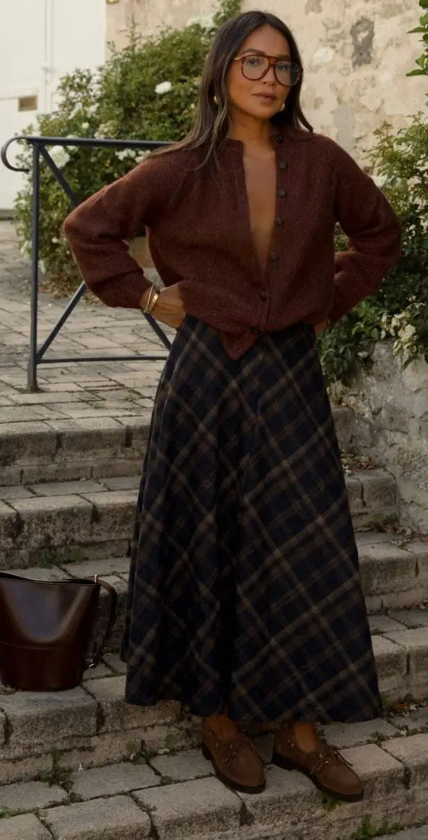 woman wearing open rust brown fine knit cardigan navy brown plaid wool maxi skirt brown suede loafers dark leather bucket bag oversized aviator glasses outdoor stone steps outfit 8
