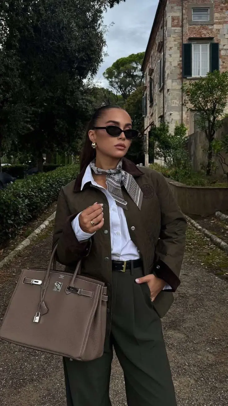 woman wearing dark olive waxed field jacket white shirt olive wide leg trousers printed silk neck scarf mini oval sunglasses large taupe structured bag gold hoop earrings outfit 9