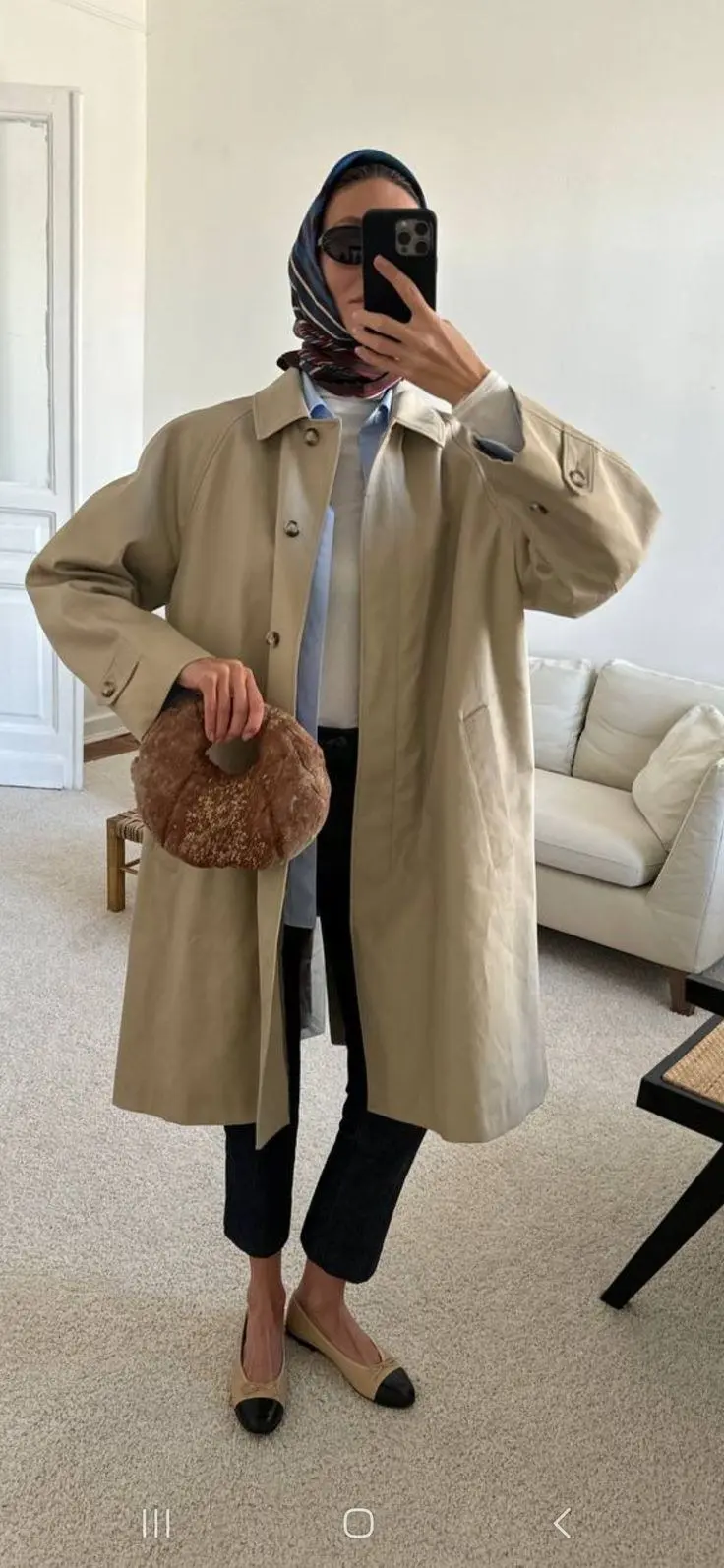 woman wearing long beige single breasted mac coat light blue collared shirt printed silk head scarf dark slim jeans fuzzy circular clutch bag cap toe ballet flats mirror selfie outfit 10