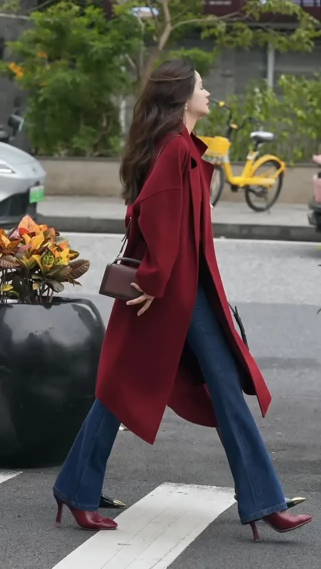 woman walking street wearing deep red wine long wool coat open flare wide leg medium wash jeans deep red pointed toe gold tip kitten heel shoes small dark red box bag outfit 15