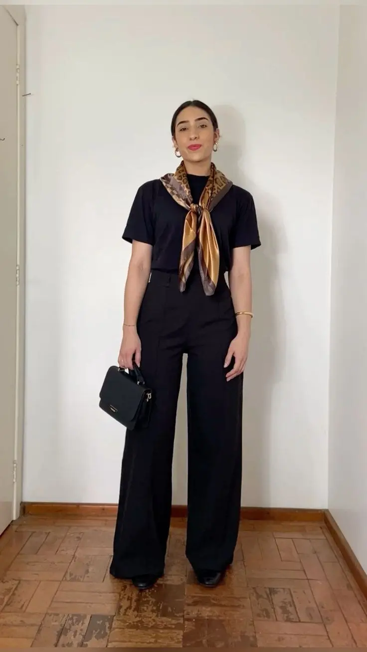 woman wearing black crewneck tee high waist wide leg black trousers black leather loafers gold brown printed satin neck scarf tied loose knot gold hoop earrings gold bangle black mini top handle bag outfit 18