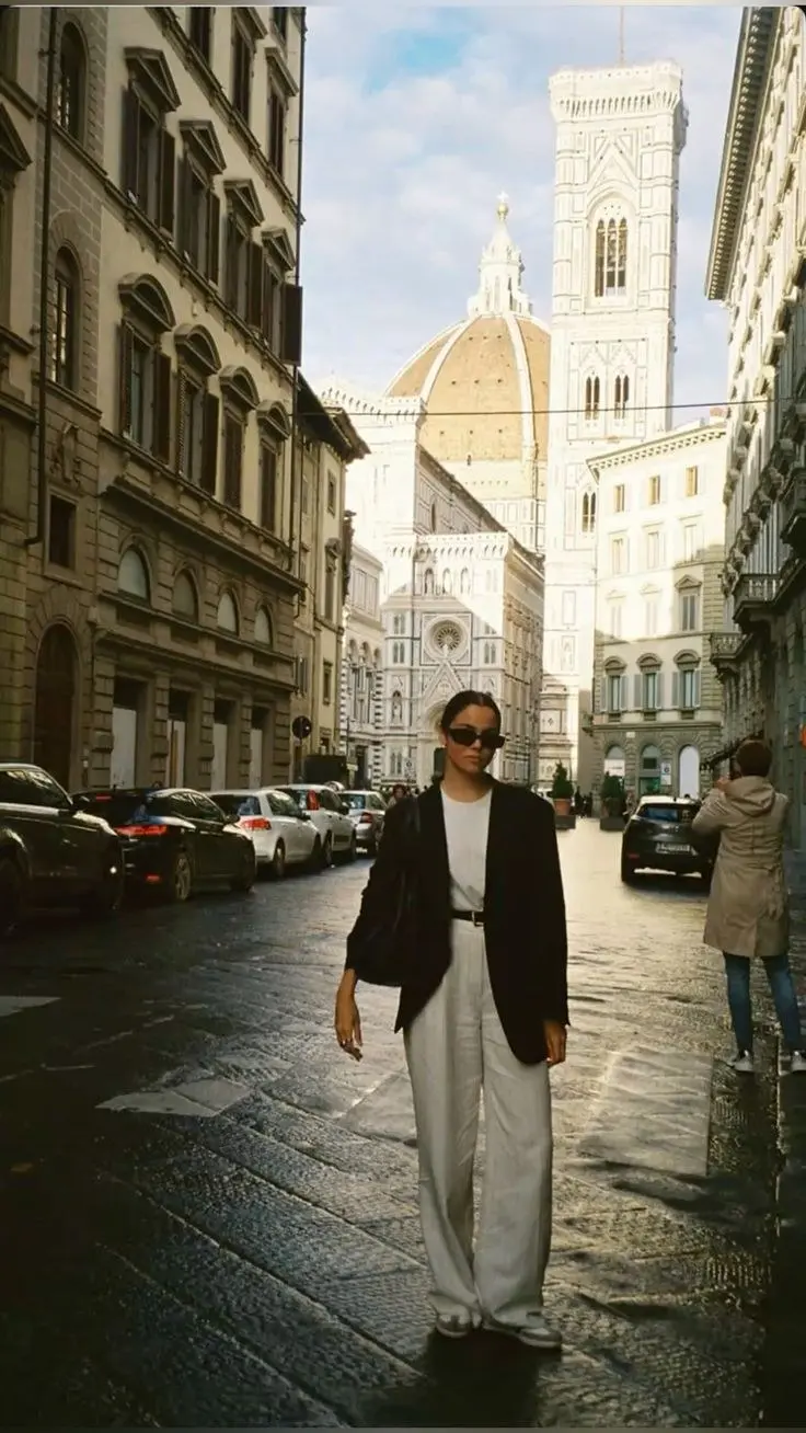 woman standing outdoor architectural background black oversized blazer white tee white wide leg trousers narrow black belt white leather sneakers dark round sunglasses low bun outfit 21