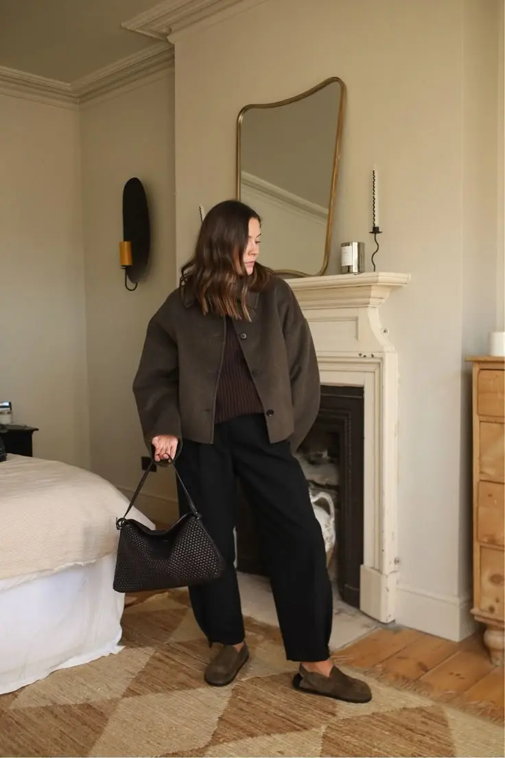 curvy woman in charcoal boxy jacket chocolate ribbed sweater black wide leg trousers olive suede loafers woven black hobo bag bedroom fireplace outfit 9