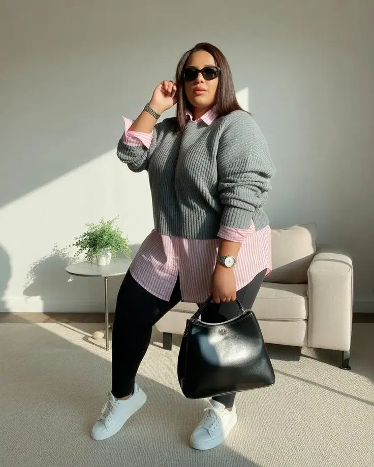curvy woman in gray ribbed sweater pink striped shirt underneath black leggings white sneakers large black structured bag sunglasses indoor natural light outfit 13