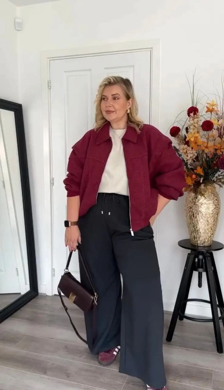 curvy woman in burgundy boxy textured jacket cream sweatshirt black wide leg drawstring trousers burgundy furry slides dark crossbody bag indoor outfit 16
