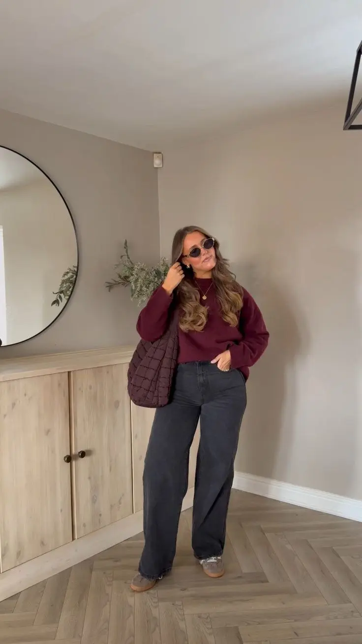 curvy woman in burgundy oversized crewneck sweater charcoal wide leg jeans gray suede platform loafers burgundy quilted oversized bag round sunglasses gold necklace indoor mirror outfit 17