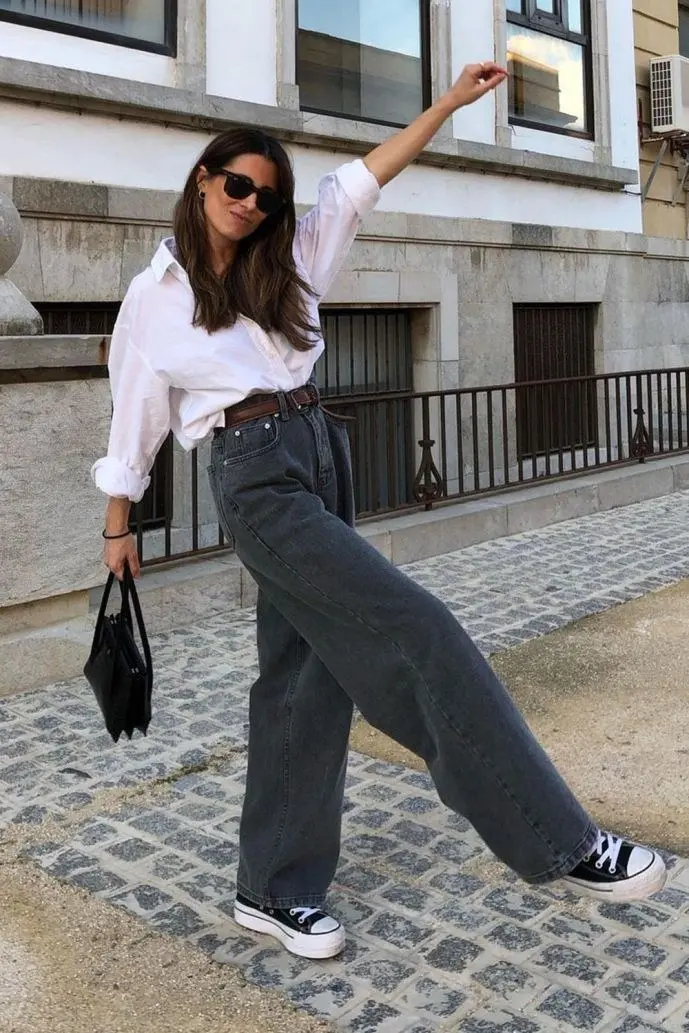 woman in white oversized shirt grey wide leg jeans brown belt black high-top sneakers black handbag sunglasses outfit 1